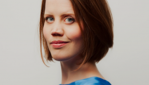 Headshot of Charlotte Forrest. Charlotte is a white woman with chin-length auburn hair and green eyes. She's wearing an aqua blue silk top.