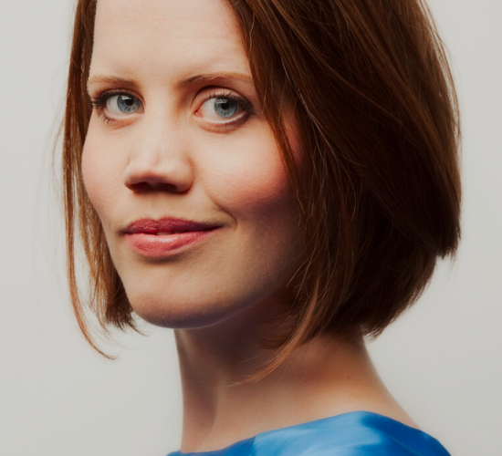 Headshot of Charlotte Forrest. Charlotte is a white woman with chin-length auburn hair and green eyes. She's wearing an aqua blue silk top.