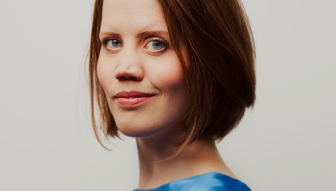 Headshot of Charlotte Forrest. Charlotte is a white woman with chin-length auburn hair and green eyes. She's wearing an aqua blue silk top.